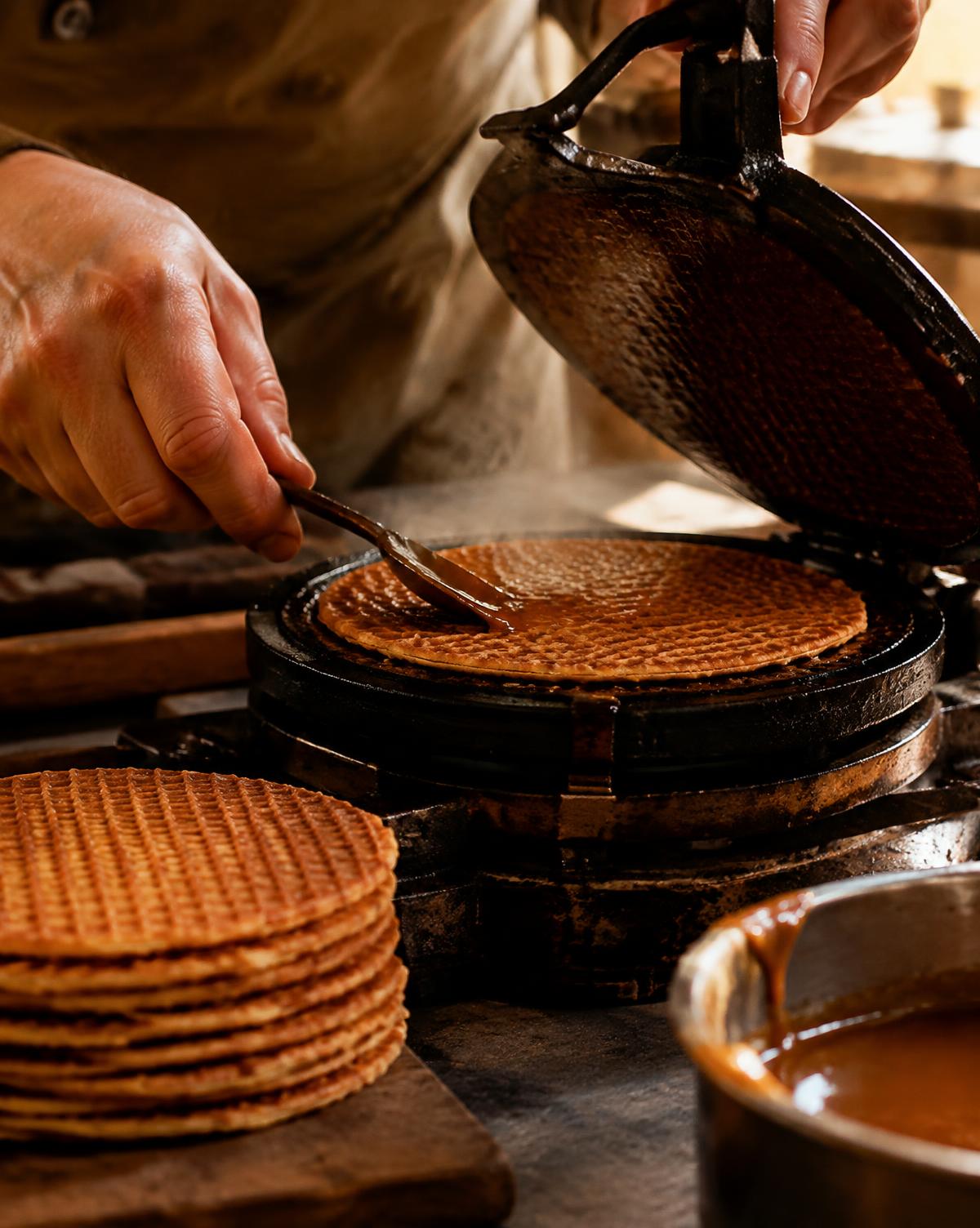 Hands spreading warm caramel syrup on a freshly pressed stroopwafel